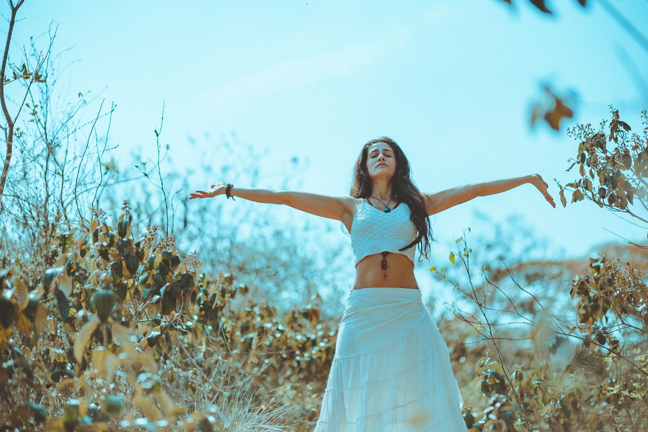 A woman in a white dress enjoying freedom and nature in a sunlit field.