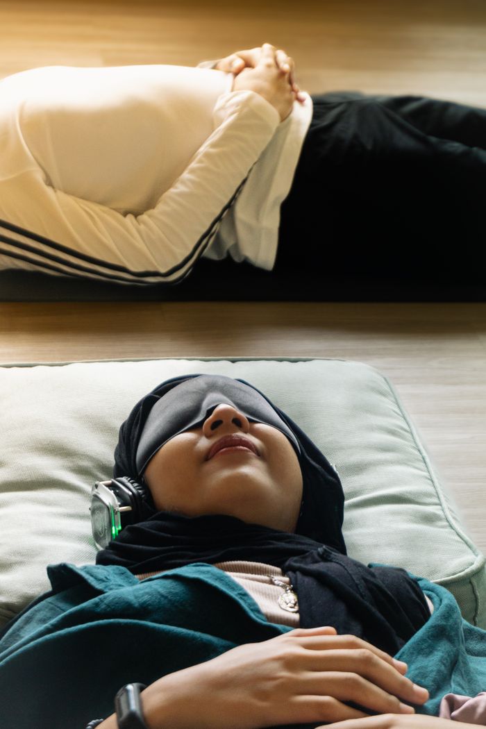 who-we-are Adults relaxing indoors with eye masks and headphones, meditating in peaceful setting.