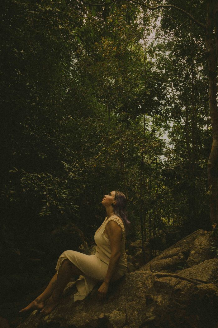 A woman seated on a rock in a lush forest under dappled light, embodying tranquility.